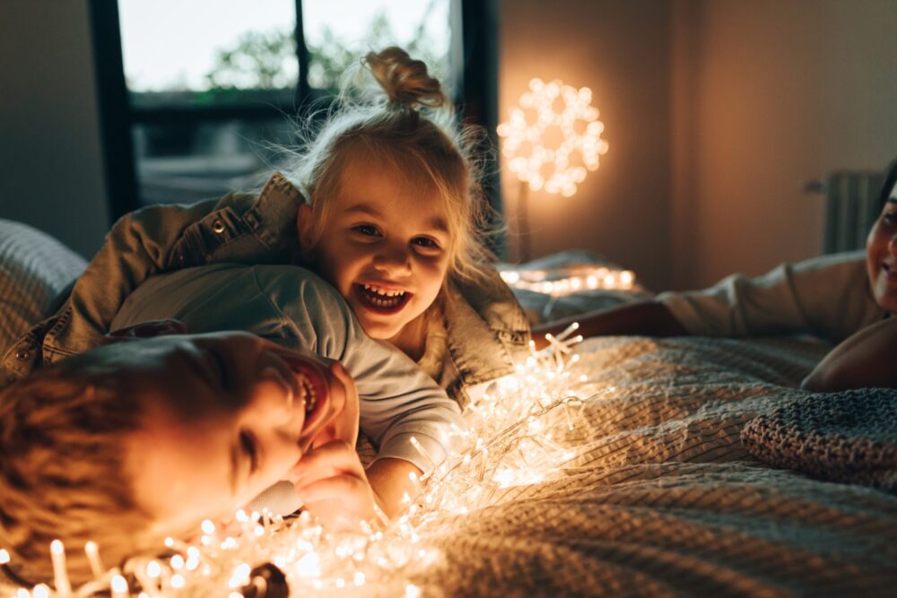 Happy children smiling on bed with Christmas string lights